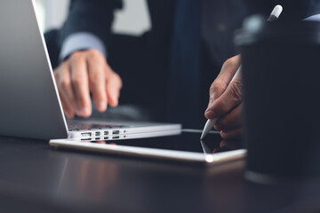 Businessman using touchscreen pen touching on digital tablet screen during working on laptop computer at office