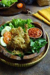 fried crispy chicken served with vegetables and sambal  in a wooden plate 
