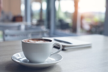 Cup of coffee and notebook on wooden table in coffee shop co-working space