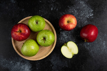Whole and sliced green and red apples on wooden plate
