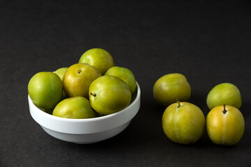 Green plums in a white ceramic saucer