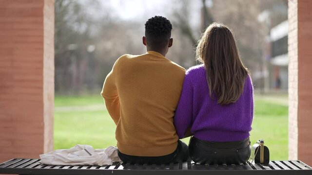 Back of interracial couple sitting on bench outside