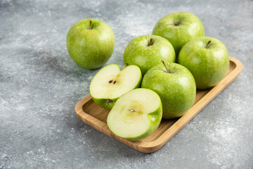 Bunch of whole and sliced green apples on wooden plate