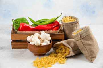Mushrooms, chili peppers and pastas in rustic basket on white background