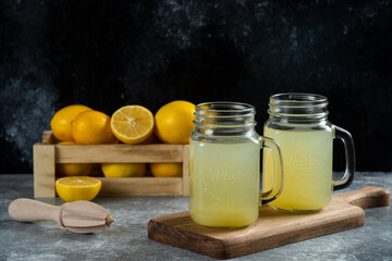 Two glass jars of tasty lemon juice and slices on a wooden board