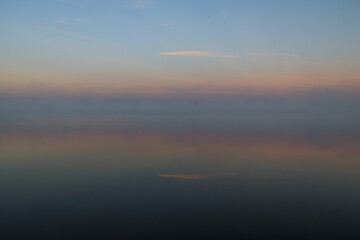 fog over the lake illuminated by the dawn sun, color gradient on fog and reflection