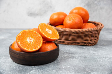 A wooden bowl full of juicy orange fruits on stone background