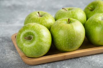 Wooden plate of shiny green apples on marble background