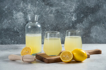 Two glass cups of lemon juice and jar on a wooden board