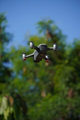 image of white and gray drone flying, with trees and sky around