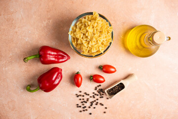 Raw pasta, vegetables and bottle of oil on orange background