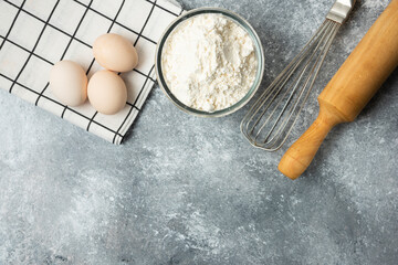 Bowl of flour, eggs and kitchen tools on marble surface