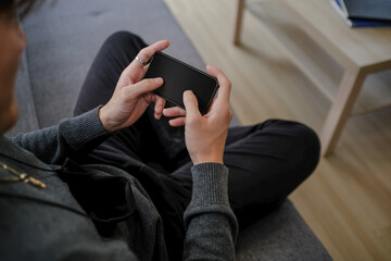 Cropped shot of young man resting on comfortable sofa and holding mobile phone.