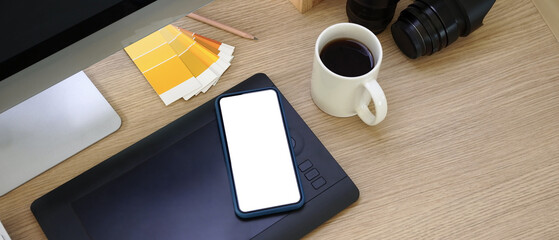 Horizontal photo of mock up smart phone with blank screen on graphic designer workplace.