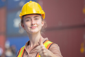 Cheerful female factory worker smiling with giving thumbs up as sign of success blurred background