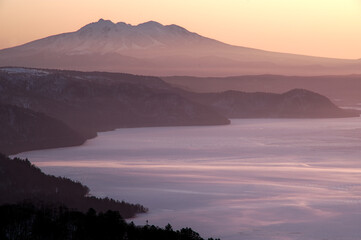 早朝の高所から見る遠くの山の稜線と眼下の湖。日本の北海道の観光地の美幌峠からの屈斜路湖と斜里岳の眺め。
