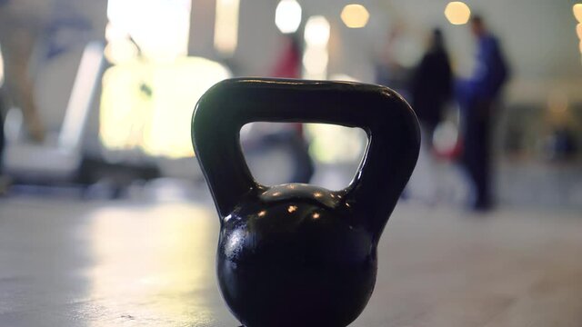 Panning shot showing a kettleball in focus with out of focus people in a gym with bright lights excercising as part of a healthy lifestyle and immunity and recovery from the coronavirus pandemic