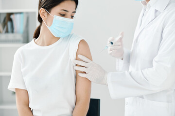 doctor in a medical gown and a mask injecting a woman in the shoulder covid vaccination