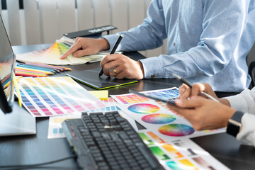 graphic designer team working on web design using color swatches editing artwork using tablet and a stylus at desks In creative office