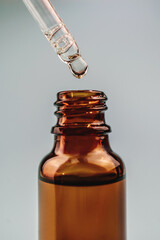 Pipette with cosmetic oil over a brown bottle