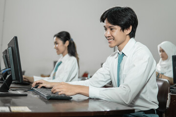 male high school students smile while using a computer pc with their friends studying
