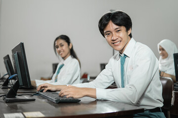 Obraz premium Male high school students smile looking at the camera while using a computer PC with their friends