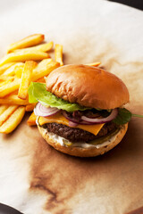 Tasty home made burger served with crispy fries. Rustic hamburger and potato chips composition with baking paper and wooden table. 
