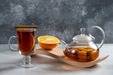 A teapot with tea and slice of orange on a wooden board