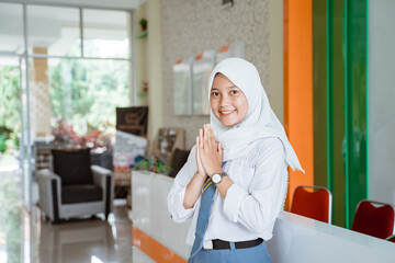 a female student wearing a headscarf high school smiles looking at the camera with a welcome hands gesture