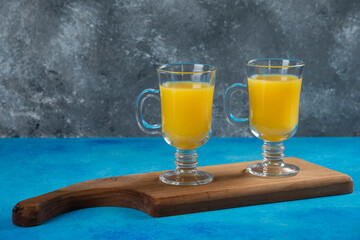Two glass cups of fresh orange juice on a wooden board