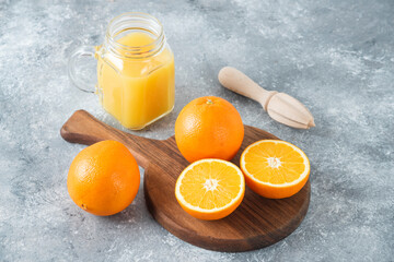 A glass pitcher of juice with fresh orange fruits on stone background
