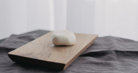 sliced mozzarella ball on olive wood board with window on background