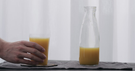 man hand take orange juice from glass bottle to tumbler glass on black wood table