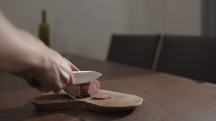 man slicing salame on olive wood board on walnut table
