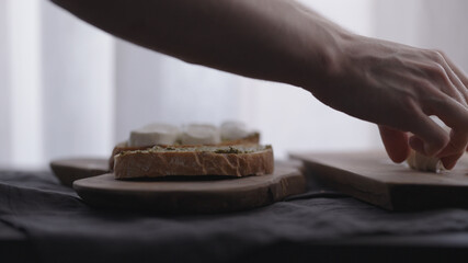 man making ciabatta bruschettas with mozzarella and pesto on olive board with window on backgorund