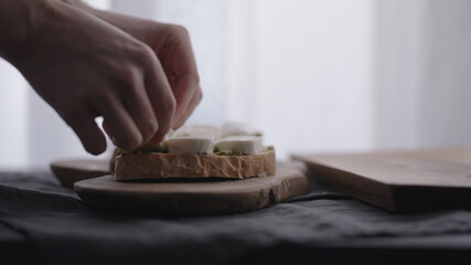 man making ciabatta bruschettas with mozzarella and pesto on olive board with window on backgorund
