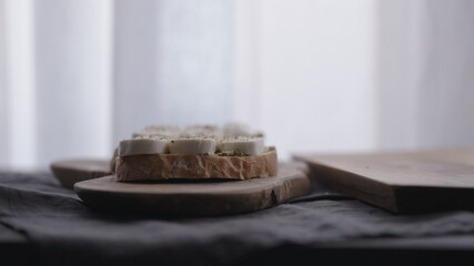 making ciabatta bruschettas with mozzarella and pesto on olive board with window on backgorund