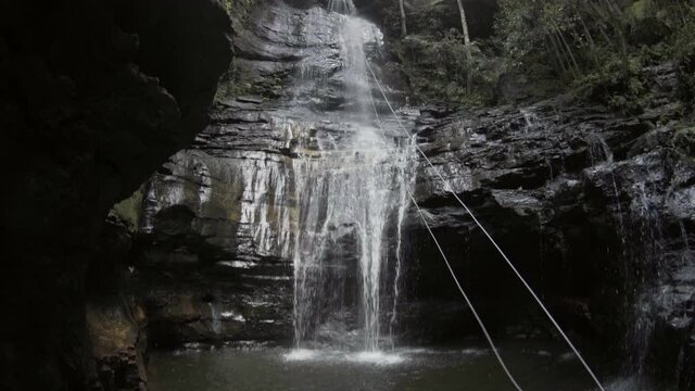 Slow Motion Tilt Up: Man With Rope By Waterfall From Rocky Cliff
