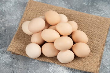 Pile of organic uncooked eggs with tablecloth on marble surface