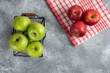 Fresh delicious green and red apples in metal basket on marble surface