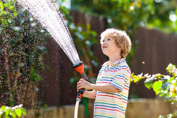 Boy watering flower in garden. Kid with water hose