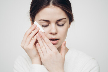 brunette woman wipes her face with a white sponge on a light background