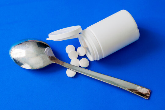 white plastic bottle with scattered pills and a tablespoon on a blue background concept medicine
