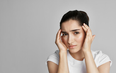 A woman in a white t-shirt holds her face with a headache and nigative health