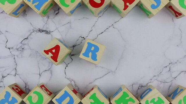 Art concept with colorful alphabet letters on wooden cubes centered between top and bottom borders of additional alphabet blocks on a marble background. Stop motion, top view
