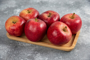 Wooden plate of shiny red apples on marble background