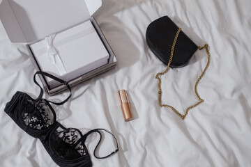 Fashionable woman flatlay on white. bed sheets. Accessories, beauty product, black purse, bra, intimate, luxurios, glamorious blogging concept, copy space