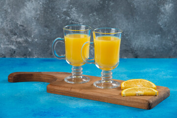 Two glass cups of orange juice on a wooden board