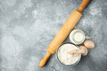 Flour, eggs, milk and rolling pin on marble background