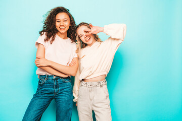 Two young beautiful smiling international hipster female in trendy summer clothes. Sexy carefree women posing near blue wall in studio. Positive models having fun. Concept of friendship